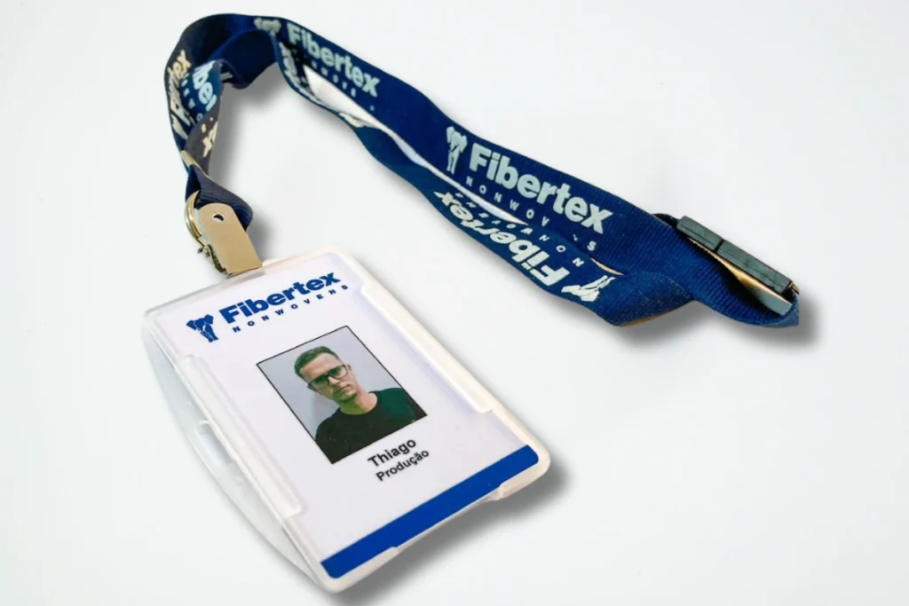 Crachá personalizado da empresa Fibertex com identificação do colaborador Thiago e cordão azul com logo institucional.